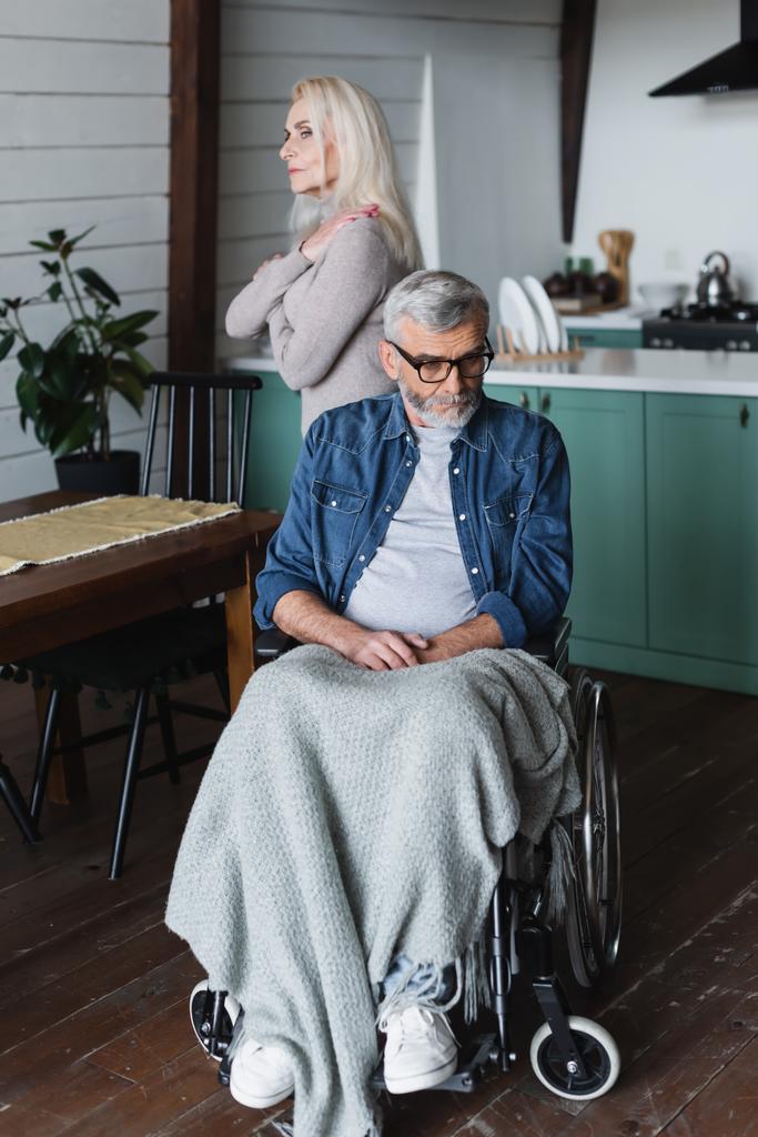 Nespokojený muž na invalidním vozíku odvrací pohled od manželky na rozmazaném pozadí  - Fotografie, Obrázek