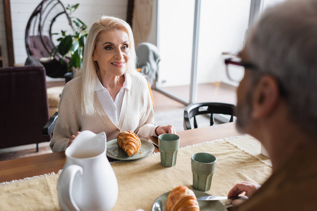 Mosolygó idős nő néz elmosódott férj mellett reggeli  - Fotó, kép