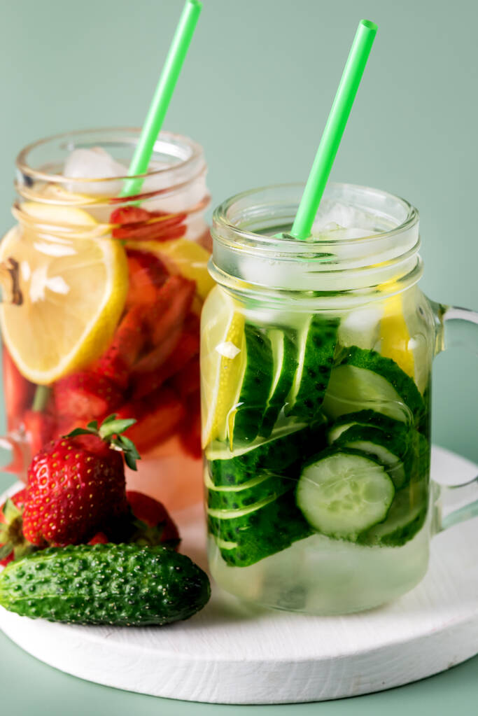 ガラス瓶の中の冷たい夏の飲み物の多様性キュウリレモンとストロベリー健康的なドリンクとデトックス水を注入緑の背景を閉じる - 写真・画像