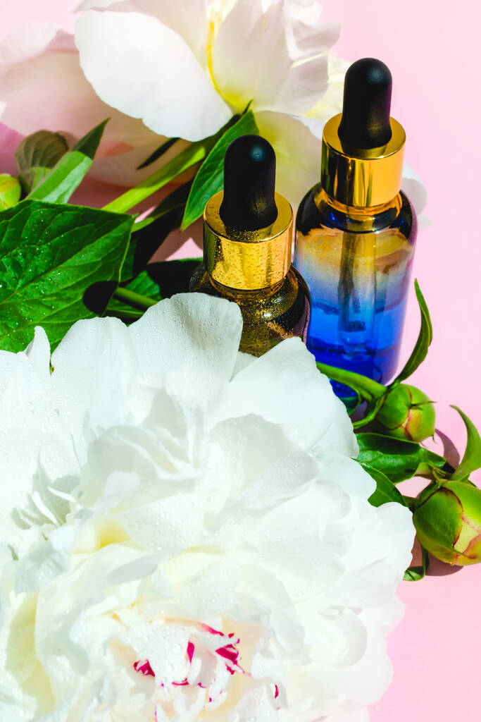 天然化粧品植物や牡丹の花、トップビューとピンクの淡い背景にピペットボトル。有機美容液、液体顔油。花の化粧品、植物の香りのコンセプト - 写真・画像