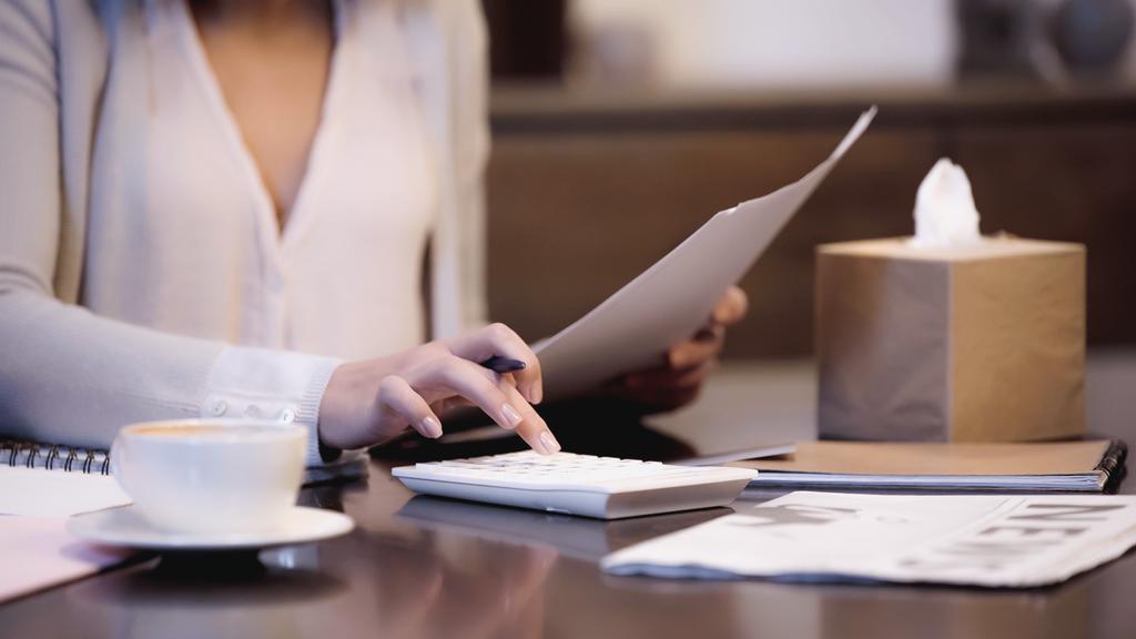 visão parcial da mulher sentada na mesa com documentos e contando com calculadora com dedo em casa - Foto, Imagem