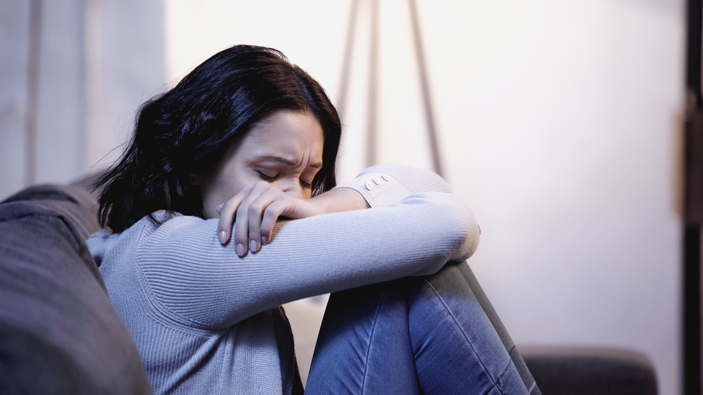 upset woman in casual clothes crying on sofa and hiding face in crossed arms at home - Photo, Image
