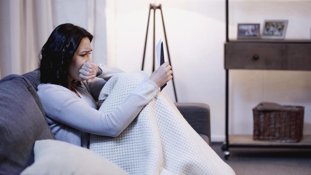 rozrušený žena pokrytá dekou sedí na pohovce s obálkou a pláče s rukou u úst doma - Fotografie, Obrázek
