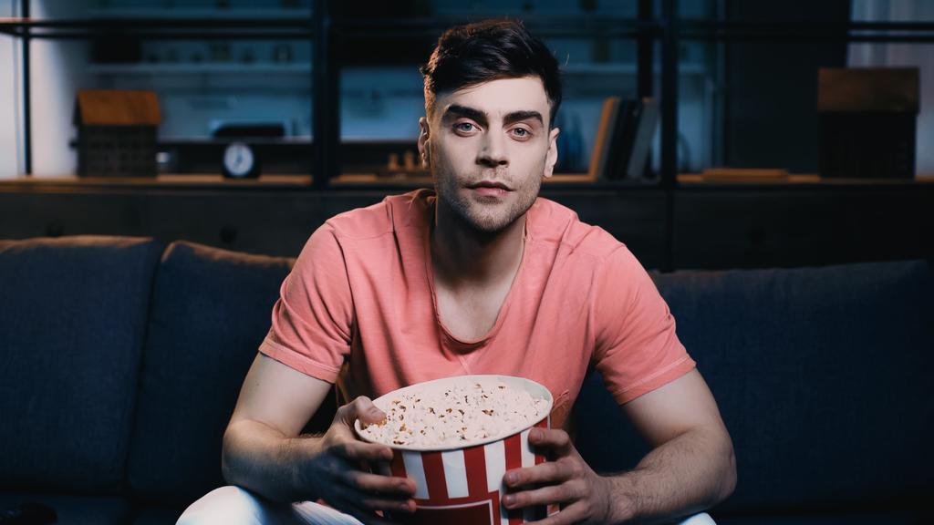 hyvännäköinen mies jolla popcorn ämpäri kun katsot elokuvaa kotona  - Valokuva, kuva