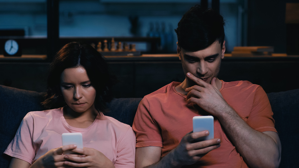 pensive man en vrouw berichten op mobiele telefoons in de moderne woonkamer  - Foto, afbeelding