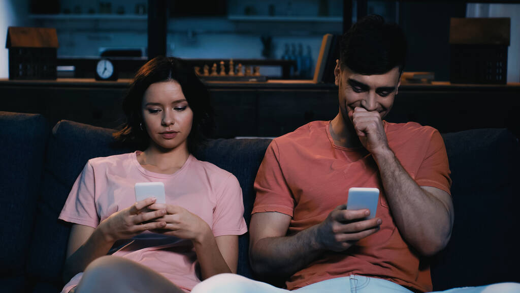 чоловік прикриває обличчя під час сміху і смс на мобільний телефон біля дівчини в сучасній вітальні
  - Фото, зображення