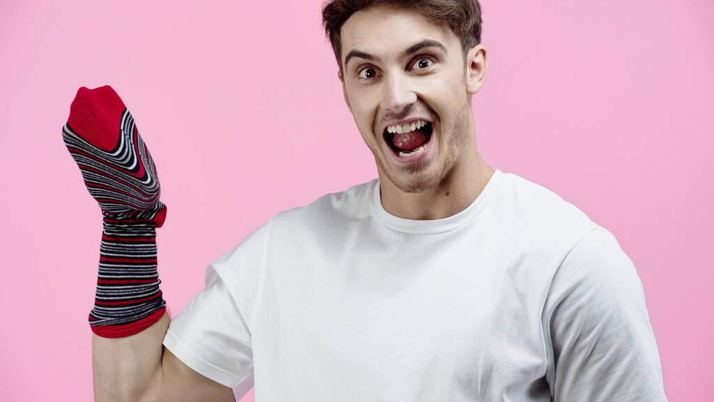Homme étonnant avec chaussette à portée de main regardant la caméra isolée sur rose  - Photo, image