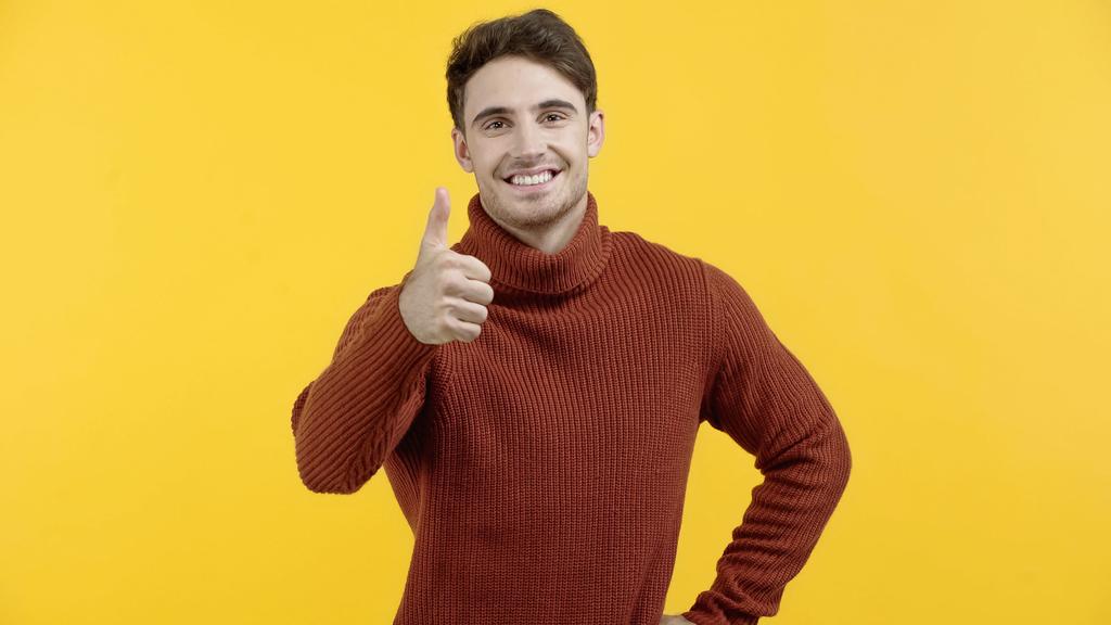 Pozitivní muž ve svetru ukazuje jako izolovaný na žluté  - Fotografie, Obrázek