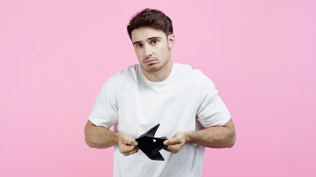 Displeased man showing empty wallet isolated on pink  - Photo, Image
