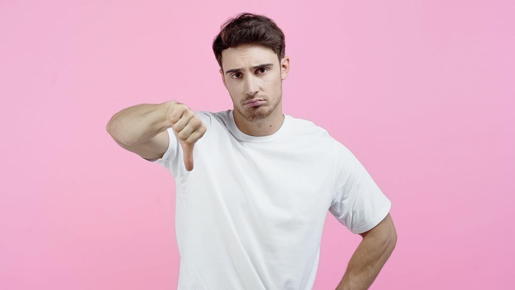 Hombre triste en camiseta blanca mostrando aversión aislada en rosa - Foto, imagen