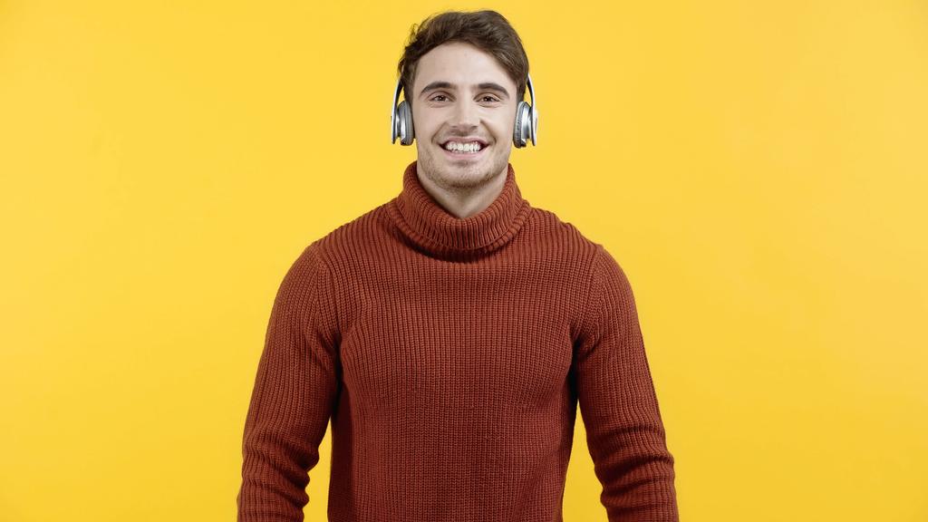 Goed uitziende man in koptelefoon glimlachend naar camera geïsoleerd op geel  - Foto, afbeelding