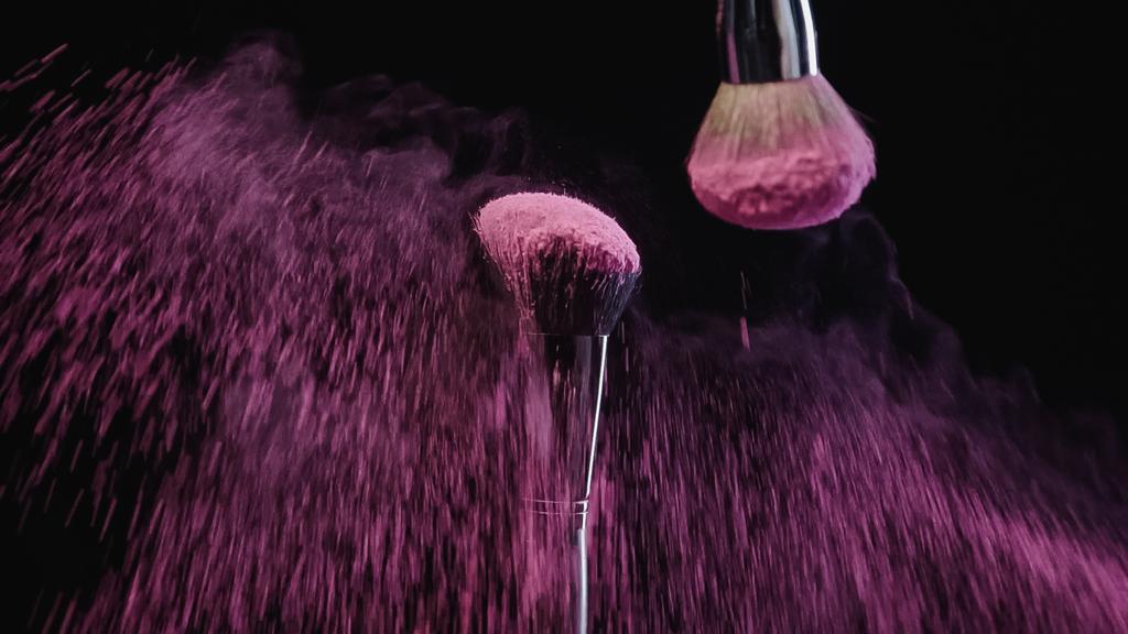 cepillos cosméticos con polvo de holi rosa sobre negro  - Foto, Imagen