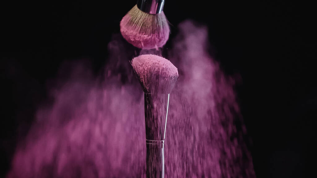 cepillos cosméticos con polvo de holi rosa cayendo sobre negro  - Foto, imagen