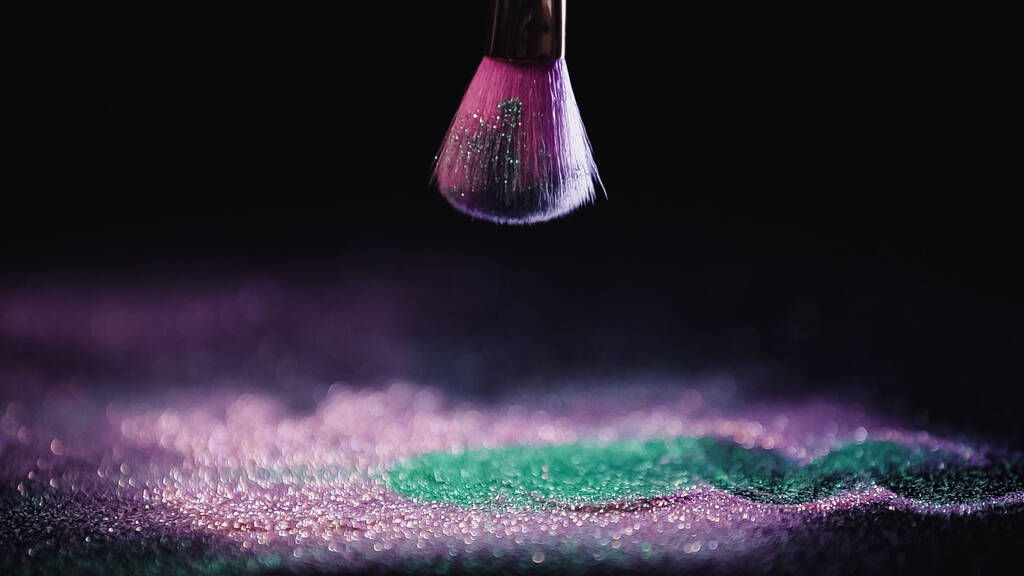cosmetic brush above shiny pink and turquoise dust on black background - Photo, Image