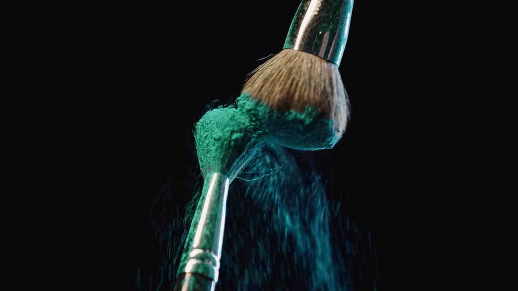 πινέλα καλλυντικά χτυπώντας και κάνοντας πιτσιλιές από μπλε χρώμα holi σε μαύρο φόντο - Φωτογραφία, εικόνα