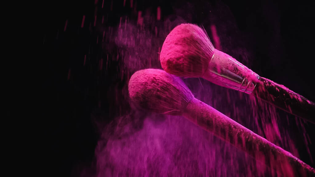 zachte cosmetische borstels maken explosie van roze poeder op zwarte achtergrond - Foto, afbeelding