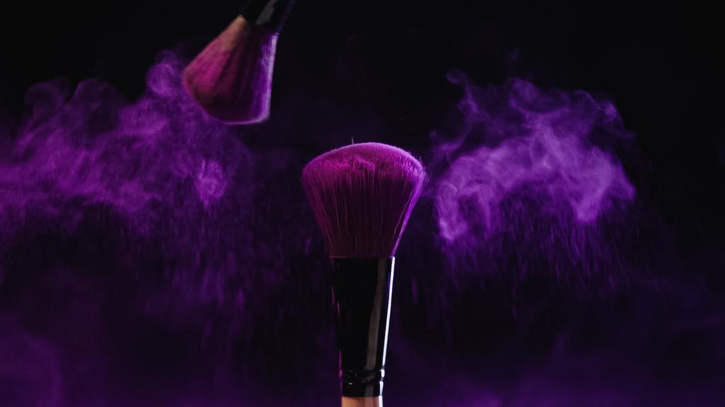 косметические кисти с фиолетовым порошком палочки возле пыли на черном фоне - Фото, изображение