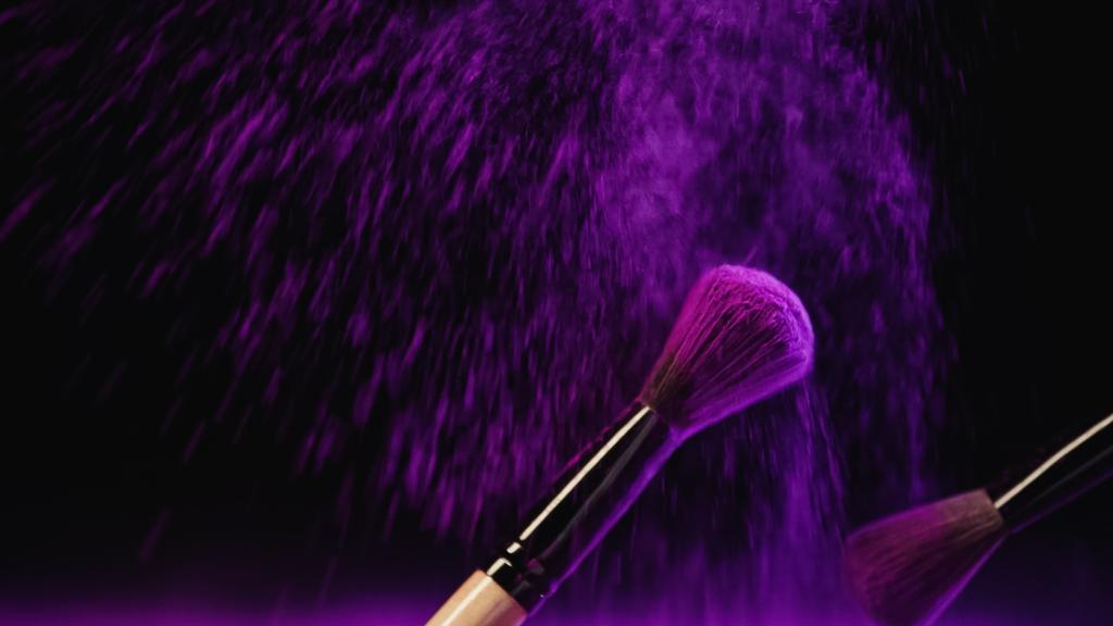 cepillos cosméticos con polvo de holi púrpura cerca del polvo salpicando sobre fondo negro - Foto, Imagen