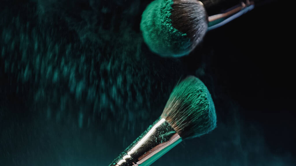 Parlak turkuaz holi boyalı kozmetik fırçalar. Koyu arkaplanda toz bulutu var. - Fotoğraf, Görsel