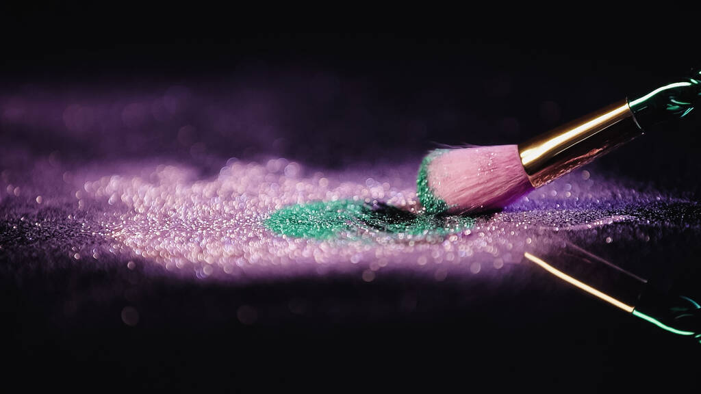 cepillo cosmético cerca de polvo brillante rosa y turquesa sobre fondo negro - Foto, Imagen