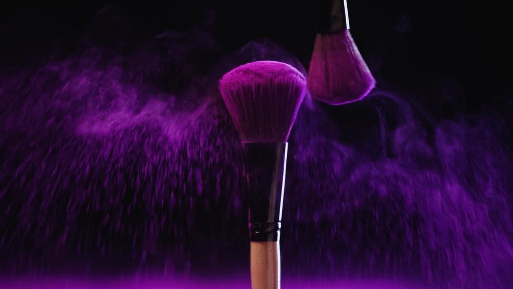 Siyah arka planda pembe toz damlalarının yanında Holi boyasıyla parlak kozmetik fırçalar. - Fotoğraf, Görsel