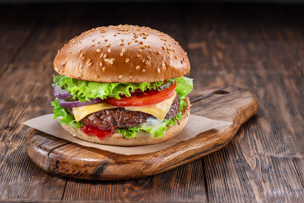 Delizioso hamburger su un tavolo di legno con uno sfondo marrone scuro dietro. Concetto fast food. - Foto, immagini