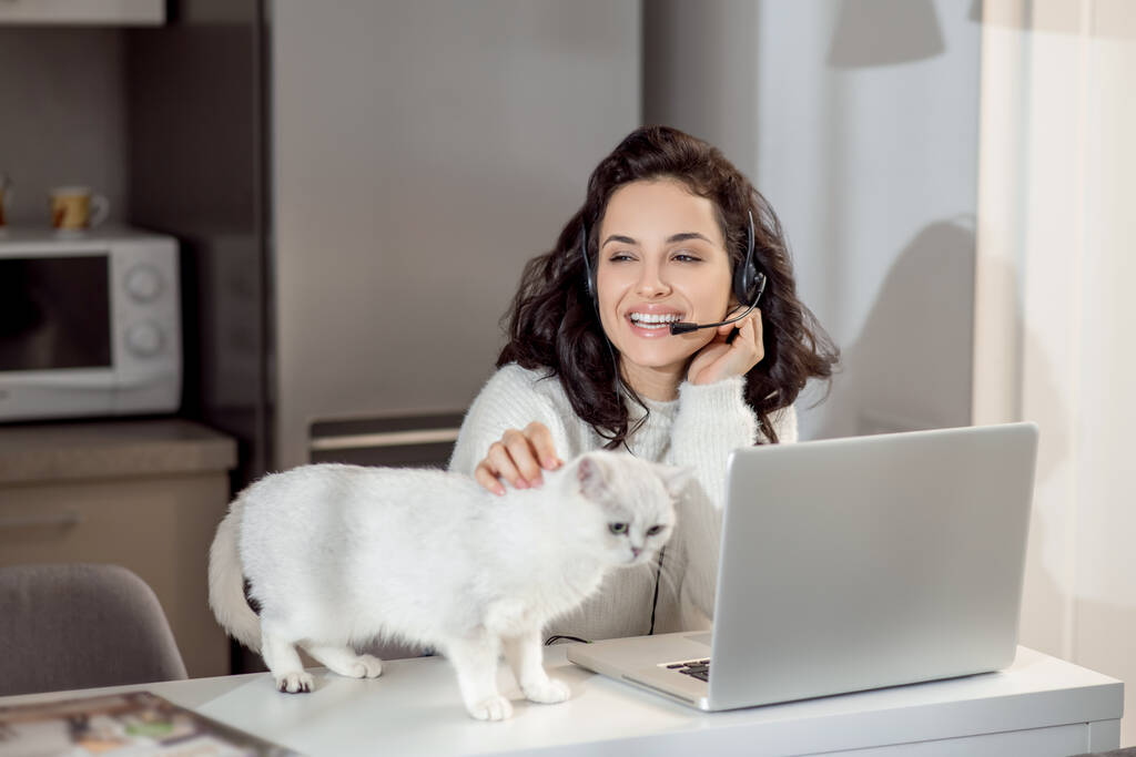 Uma mulher em fones de ouvido sentada no laptop enquanto trabalhava em casa - Foto, Imagem