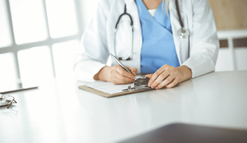 Неизвестная женщина-врач на работе заполняет в клинике анкету с записями о лекарствах, крупным планом - Фото, изображение