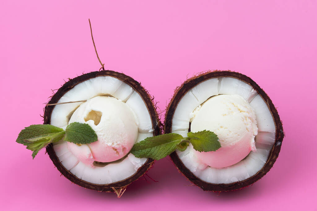 Vanília fagylaltgolyó friss kókuszdió felében mentalevéllel díszítve rózsaszín alapon. - Fotó, kép