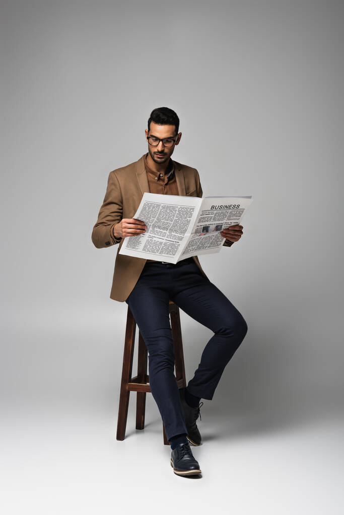Арабский бизнесмен читает деловые новости на стуле на сером фоне - Фото, изображение