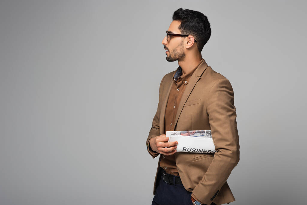 Vista lateral del empresario musulmán sosteniendo periódico aislado en gris  - Foto, Imagen