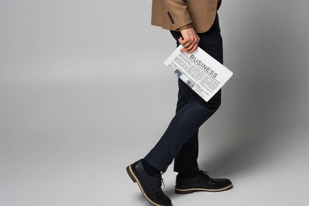 Cropped view of newspaper with business lettering in hand of man in suit on grey background - Foto, afbeelding