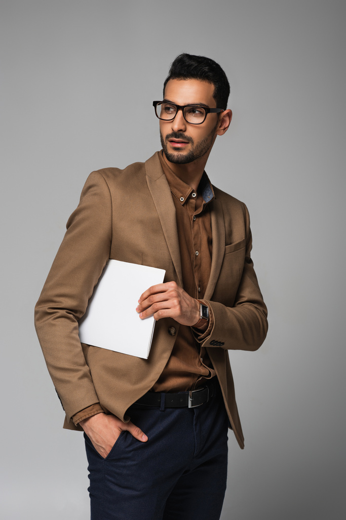 Молодой мусульманский бизнесмен в очках держит бумаги, изолированные на сером  - Фото, изображение