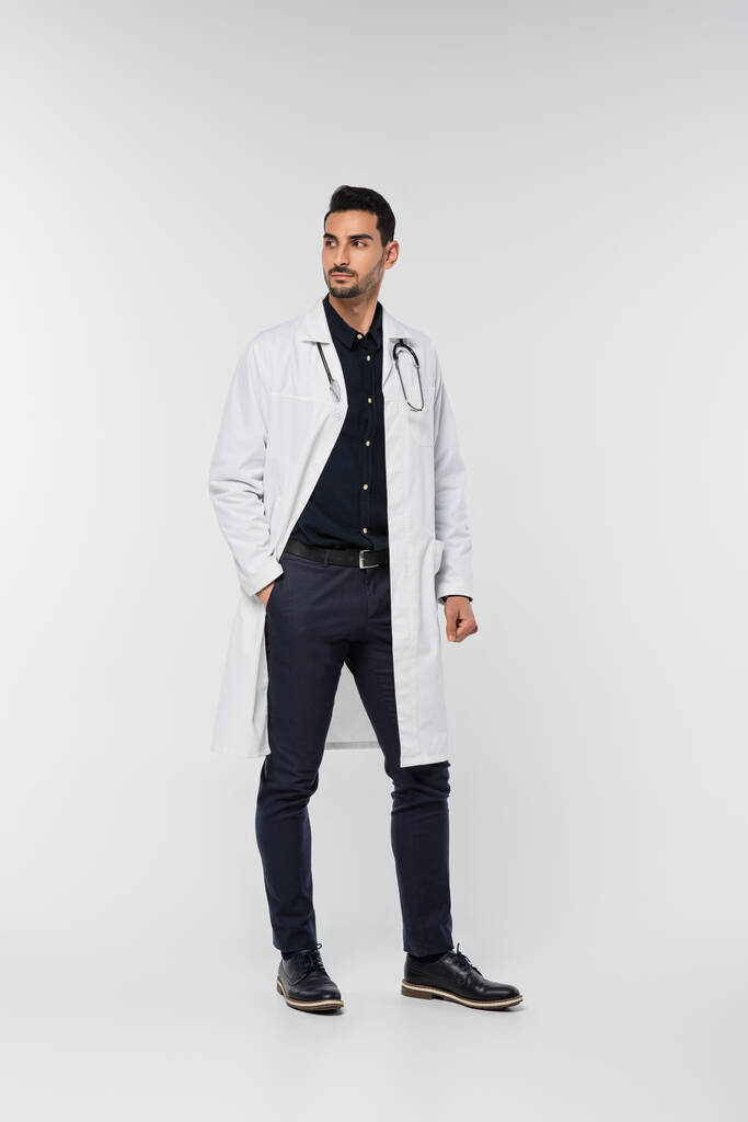 Arabischer Arzt im weißen Mantel schaut auf grauem Hintergrund weg - Foto, Bild