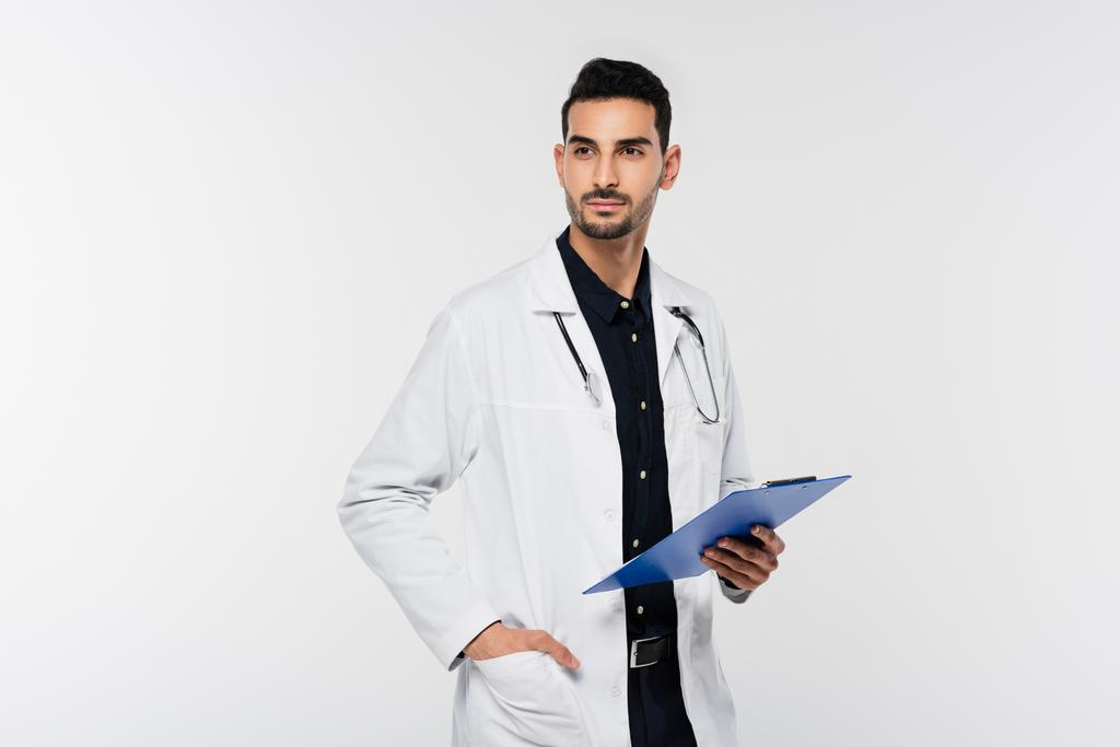 Médico musulmán con portapapeles mirando hacia otro lado aislado en gris  - Foto, Imagen