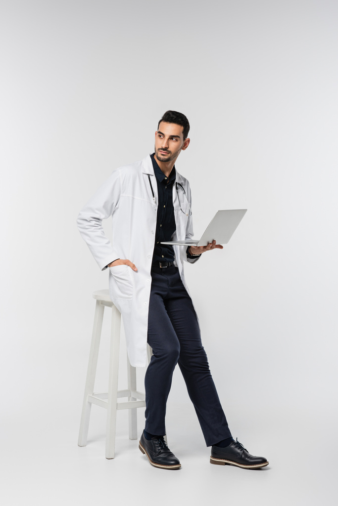 Muslim doctor with laptop looking away on grey background  - Foto, afbeelding