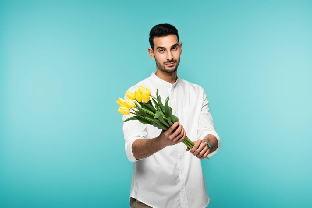 Muslim man in white shirt holding flowers isolated on blue  - Photo, Image