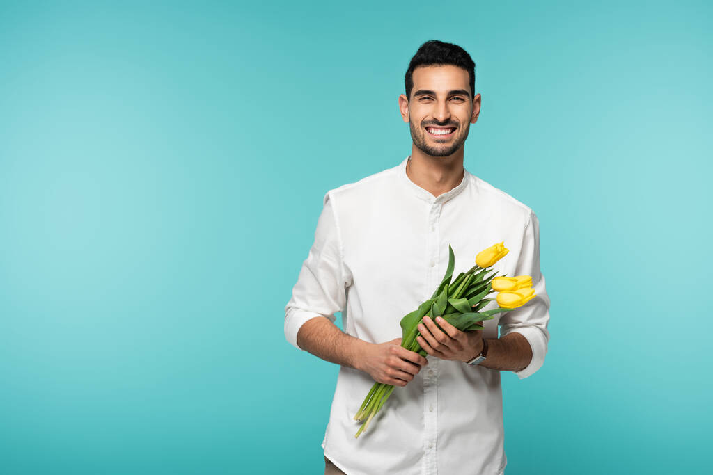 Позитивний арабський чоловік тримає квіти тюльпанів ізольовані на синьому
  - Фото, зображення