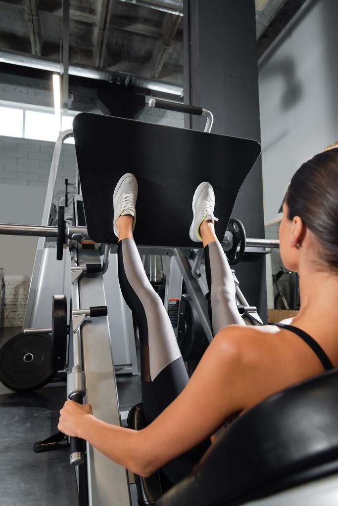 vista posterior de la deportista haciendo ejercicio en la máquina de ejercicio de extensión de pierna - Foto, Imagen