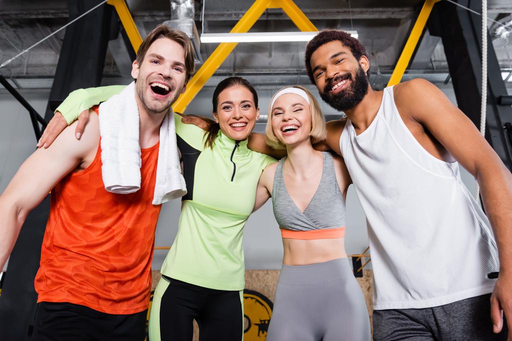 cheerful multiethnic people looking at camera while embracing in gym - Photo, Image