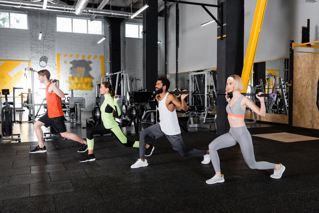 young multiethnic sports people doing forward lunges with gymnastic sticks  - Photo, Image