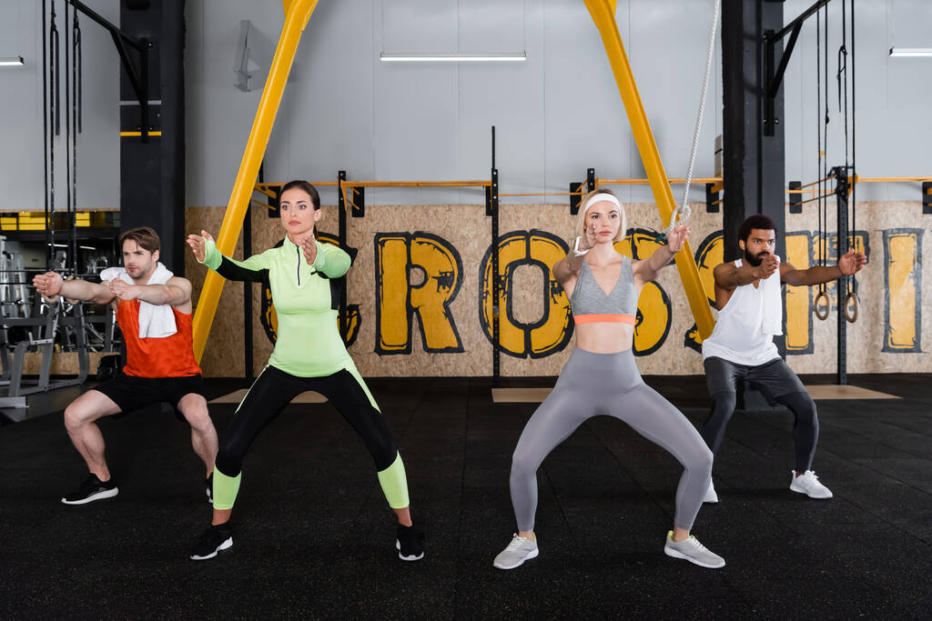 межрасовые спортивные люди тренируются в неловкой позе йоги в тренажерном зале - Фото, изображение