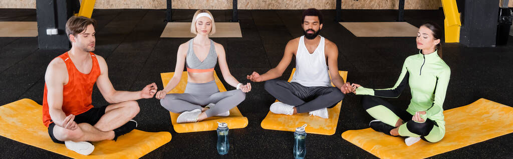 młodych międzyrasowych ludzi w odzieży sportowej medytujących w pozycji lotosu, baner - Zdjęcie, obraz