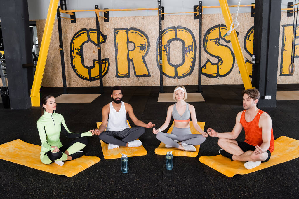 personnes multiethniques méditant dans la pose du lotus avec les yeux fermés sur les tapis de fitness - Photo, image