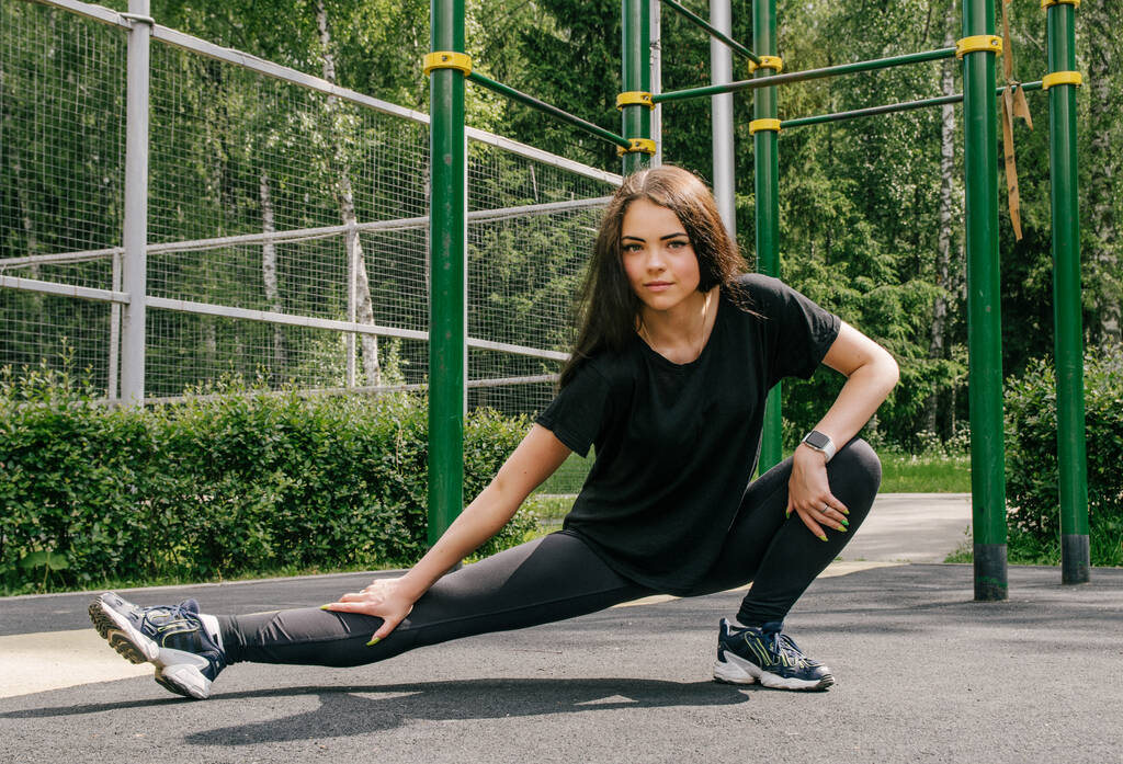 una ragazza in una maglietta nera e leggings è impegnata in gamba sportiva  - Foto, immagini