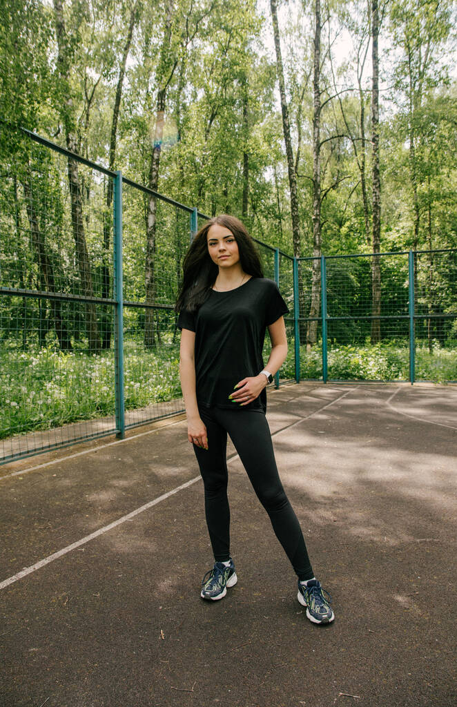 Ein Mädchen in schwarzem T-Shirt und Leggings steht im Sommer auf einem Basketballplatz - Foto, Bild