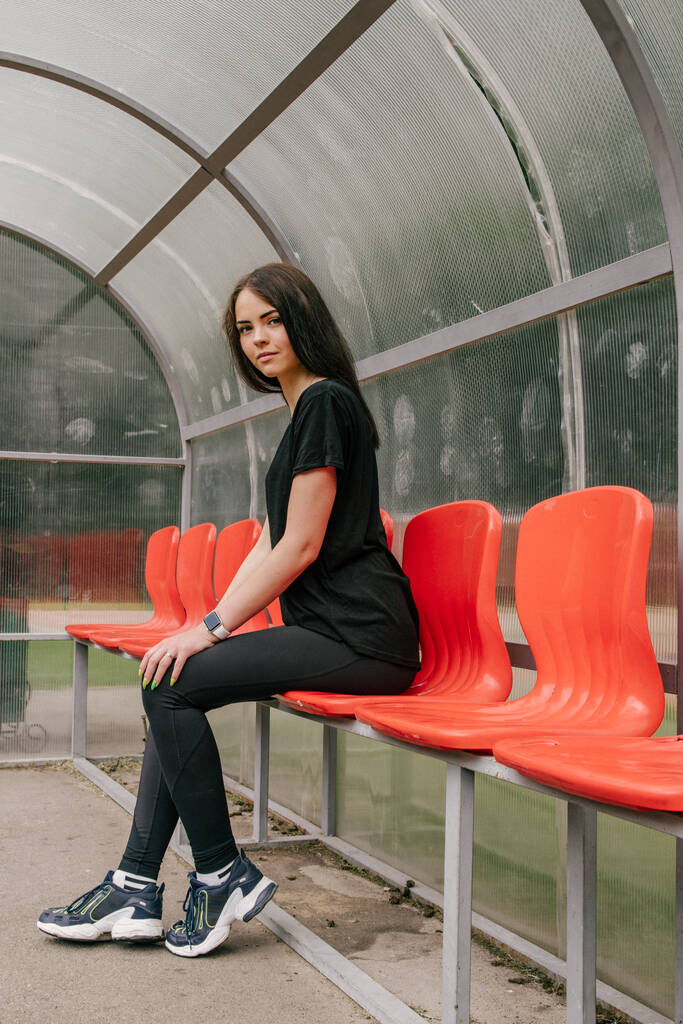 a girl in a black T-shirt and leggings sits on the seats for the - Photo, Image