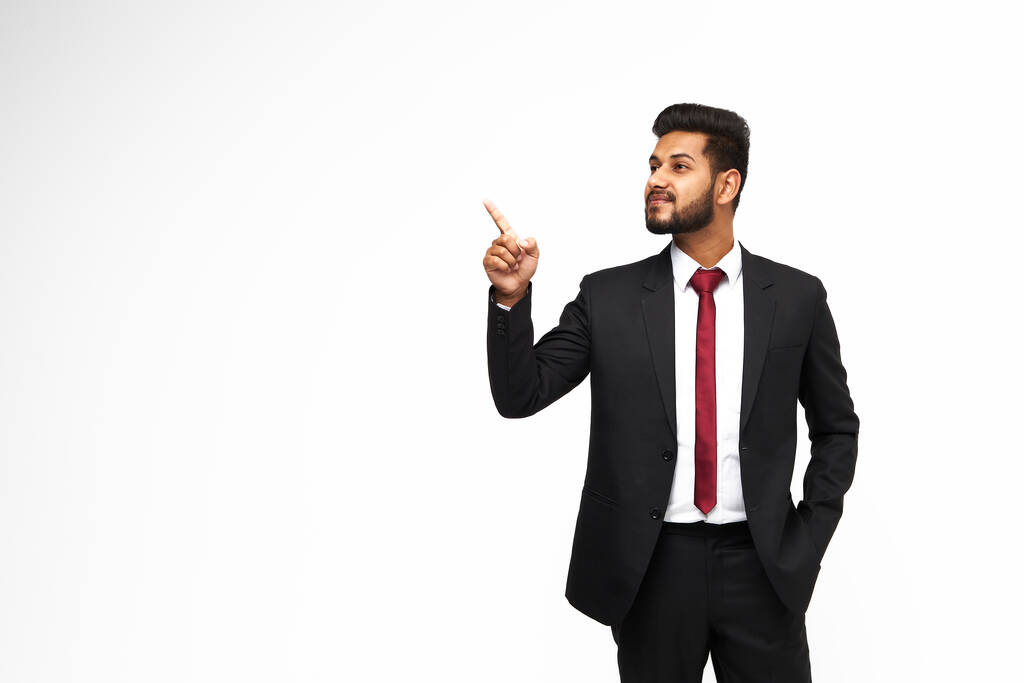 Jonge, stijlvolle indiaanse manager in een klassiek pak wijst zijn vinger op een witte geïsoleerde achtergrond, kopieer ruimte voor tekst. - Foto, afbeelding