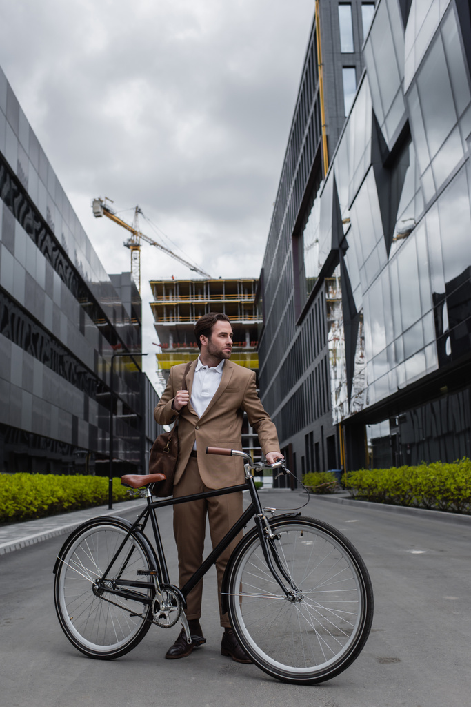 comprimento total do homem de negócios em terno segurando saco e de pé perto da bicicleta fora  - Foto, Imagem