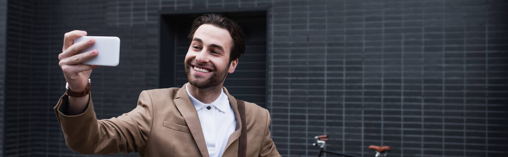 счастливый молодой бизнесмен в формальной одежде делает селфи по сотовому телефону снаружи, баннер - Фото, изображение